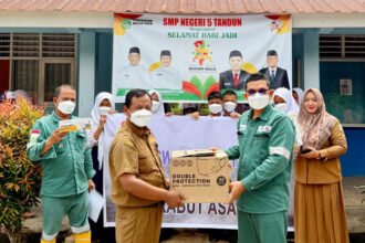 Rafiq Adriansyah selaku Head of Field Support dan Supriadi selaku Public & Government Relation Kingswood Capital Ltd. Menyerahkan masker kepada Irianto selaku Kepala Sekolah SMPN 5 Tandun